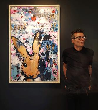 Harry Bunce, a contemporary British artist, stands beside one of his vibrant paintings featuring a large, whimsical rabbit character set against a colorful, abstract background.